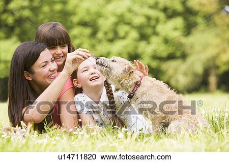 Stock Image - Mother and daughters in park with dog smiling. Fotosearch
