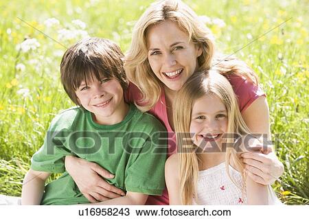 Stock Image - Mother and two young children sitting outdoors smiling. Fotosearch