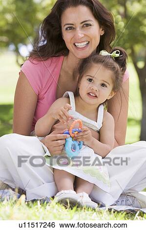 Woman and young girl sitting outdoors with toy smiling View Large Photo Image Stock Photograph - Woman and young girl sitting outdoors with toy smiling. Fotosearch