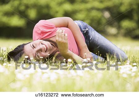 Stock Image - Woman lying outdoors with flower smiling. Fotosearch