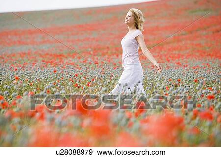 Stock Photo - Woman walking in poppy field smiling. Fotosearch