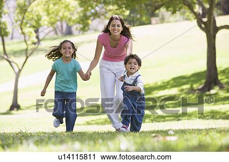 Stock Image - Woman with two young children running outdoors smiling. Fotosearch