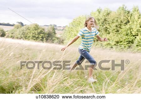 Stock Image - Young girl running in a field smiling. Fotosearch