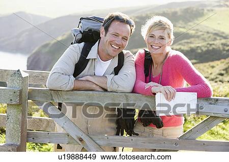 Stock Photo - Couple on cliffside outdoors leaning on railing and smiling. Fotosearch
