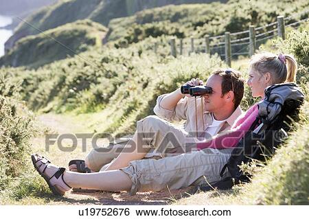 Stock Photograph - Couple on cliffside outdoors using binoculars and smiling. Fotosearch