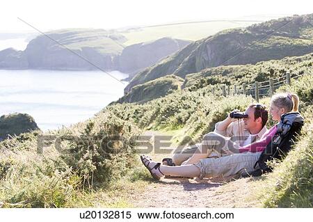 Couple on cliffside outdoors using binoculars and smiling View Large Photo Image Stock Photography - Couple on cliffside outdoors using binoculars and smiling. Fotosearch