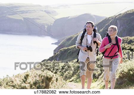 Stock Image - Couple on cliffside outdoors walking and smiling. Fotosearch
