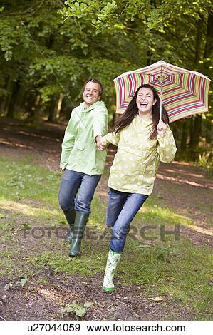 Stock Photo - Couple outdoors running with umbrella smiling. Fotosearch