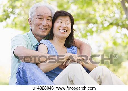 Stock Image - Couple relaxing outdoors in park smiling. Fotosearch
