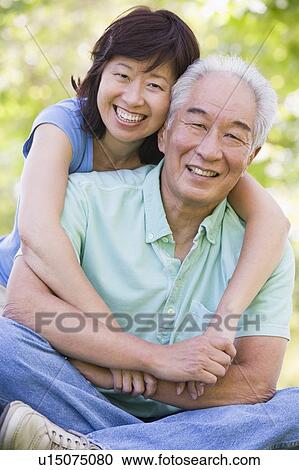 Stock Image - Couple relaxing outdoors in park smiling. Fotosearch