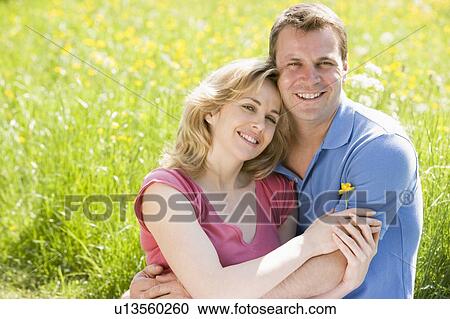 Couple sitting outdoors holding flower smiling View Large Photo Image Stock Image - Couple sitting outdoors holding flower smiling. Fotosearch
