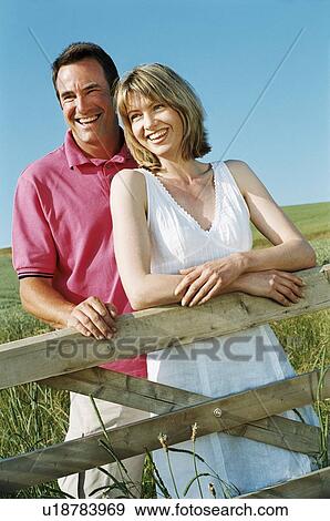 Stock Photo - Couple standing outdoors by fence smiling. Fotosearch