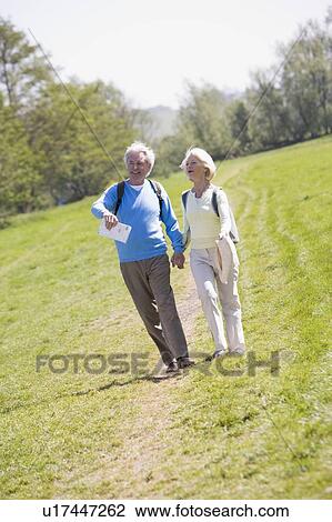 Stock Image - Couple walking on path in park holding hands and smiling. Fotosearch