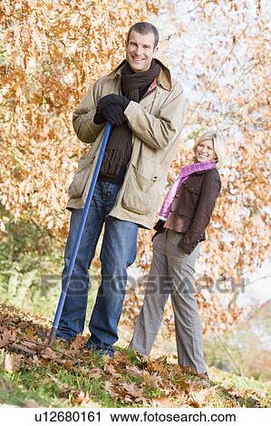 Man outdoors raking leaves and woman in background smiling (selective focus) View Large Photo Image Stock Image - Man outdoors raking leaves and woman in background smiling (selective focus). Fotosearch