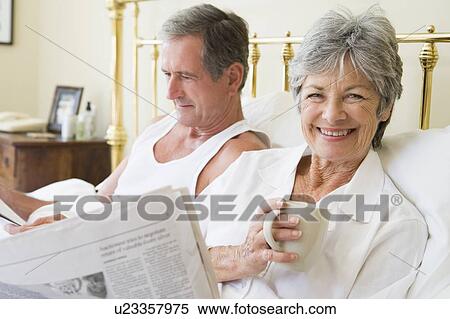 Stock Photography - Couple in bedroom with coffee and newspapers smiling. Fotosearch