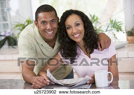 Stock Image - Couple in kitchen with newspaper and coffee smiling. Fotosearch