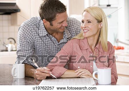 Couple in kitchen with newspaper and coffee smiling View Large Photo Image Stock Photo - Couple in kitchen with newspaper and coffee smiling. Fotosearch