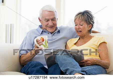 Picture - Couple in living room reading newspaper with coffee smiling. Fotosearch