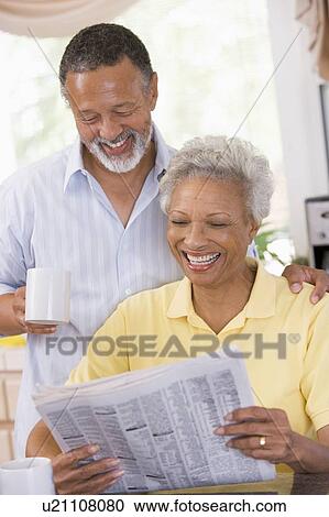 Stock Image - Couple relaxing with a newspaper smiling. Fotosearch