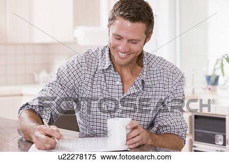 Stock Photography - Man in kitchen reading newspaper and smiling. Fotosearch