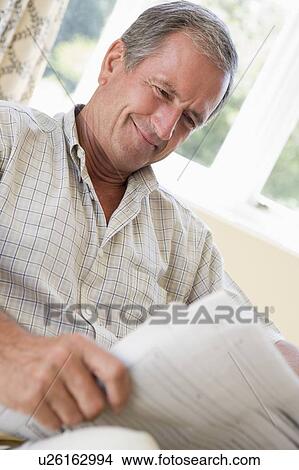 Picture - Man in living room reading newspaper smiling. Fotosearch