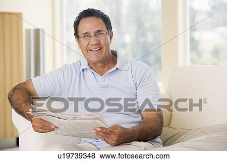 Stock Photo - Man in living room reading newspaper smiling. Fotosearch