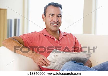 Stock Image - Man reading newspaper in living room smiling. Fotosearch