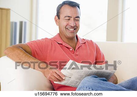 Stock Photograph - Man reading newspaper in living room smiling. Fotosearch