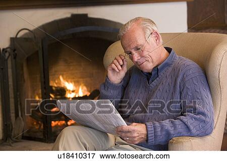 Stock Photo - Man sitting in living room by fireplace with newspaper. Fotosearch
