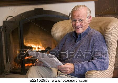Stock Photo - Man sitting in living room by fireplace with newspaper smiling. Fotosearch