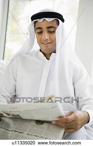 Stock Image - Man sitting indoors with newspaper smiling (high key/selective focus). Fotosearch
