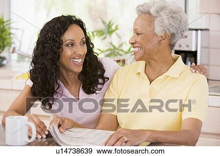 Two women in kitchen with newspaper and coffee smiling View Large Photo Image Stock Photo - Two women in kitchen with newspaper and coffee smiling. Fotosearch