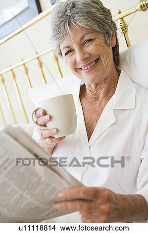 Woman in bedroom with coffee and newspaper smiling View Large Photo Image Picture - Woman in bedroom with coffee and newspaper smiling. Fotosearch