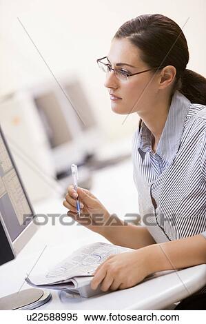 Stock Photography - Woman in computer room circling items in a newspaper. Fotosearch