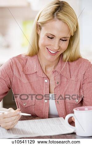 Stock Photo - Woman in kitchen with newspaper and coffee smiling. Fotosearch