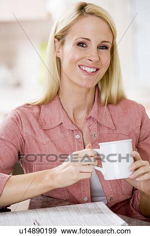 Stock Photo - Woman in kitchen with newspaper and coffee smiling. Fotosearch