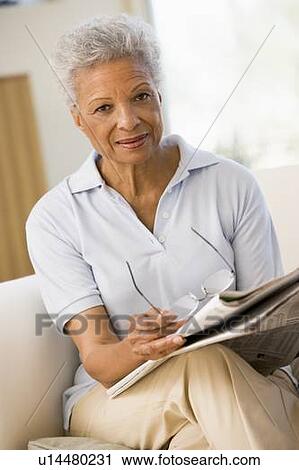 Stock Image - Woman with a newspaper holding eyeglasses. Fotosearch