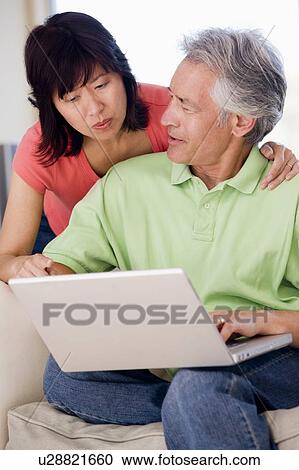 Stock Image - Couple in living room with laptop smiling. Fotosearch