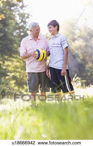 Stock Image - Grandfather and grandson at a park holding a ball and smiling. Fotosearch
