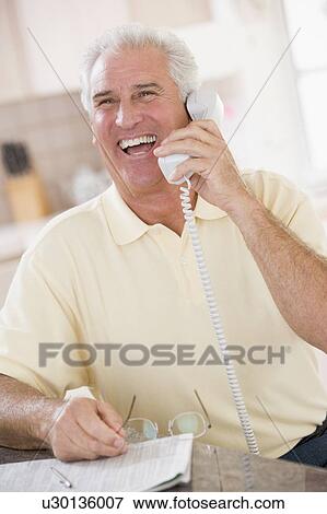 Stock Photo - Man in kitchen on telephone laughing. Fotosearch