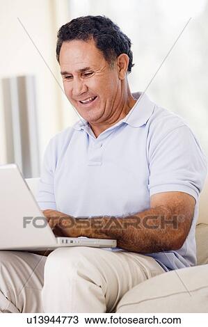 Stock Image - Man in living room with laptop smiling. Fotosearch