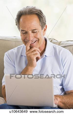 Man in living room with laptop smiling View Large Photo Image Stock Photo - Man in living room with laptop smiling. Fotosearch