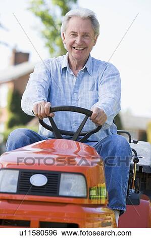 Stock Photograph - Man outdoors driving lawnmower smiling. Fotosearch
