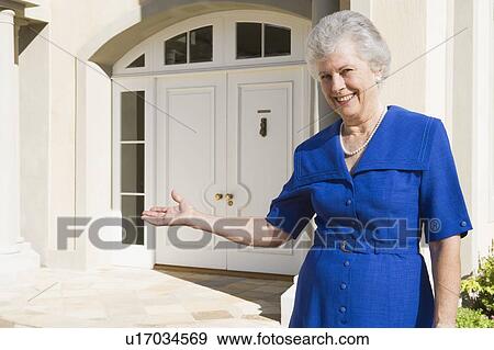 Stock Photo - Senior woman standing outside her home. Fotosearch