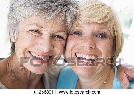 Stock Image - Two women in living room smiling. Fotosearch