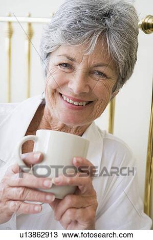Stock Image - Woman in bedroom with coffee smiling. Fotosearch