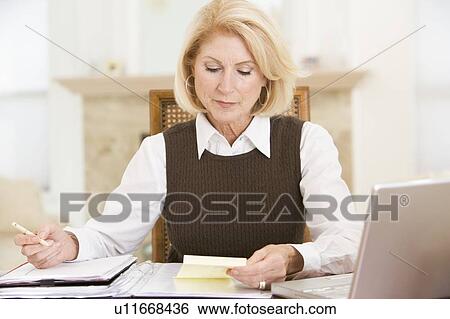Stock Photograph - Woman in dining room with laptop and paperwork. Fotosearch