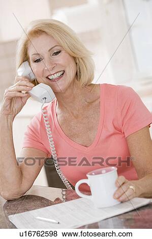 Woman in kitchen with coffee using telephone smiling View Large Photo Image Stock Photo - Woman in kitchen with coffee using telephone smiling. Fotosearch