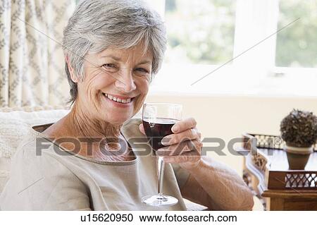 Stock Image - Woman in living room with glass of wine smiling. Fotosearch