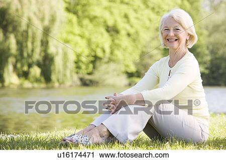 Stock Image - Woman outdoors at park by lake smiling. Fotosearch